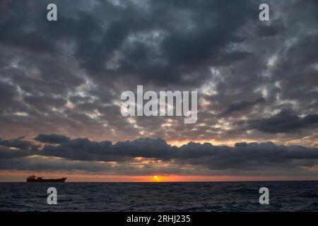 Colorful red and orange sunset with dark blue sky in the deep blue sea with ship on the background. Stock Photo