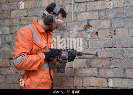 Construction worker using hammer drill with chisel to remove old cement from brick wall indoors. Stock Photo