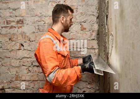 Man builder using h shape rule for plastering brick wall indoors. Stock Photo