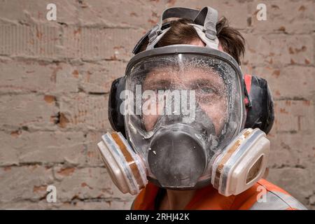 Male worker wearing full face respirator mask and ear defenders for working in hazard environment. Stock Photo
