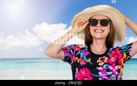 Travel banner, young smiling woman in sunglasses, sunhat and summer dress standing on Hawaii beach in front of the ocean. Stock Photo