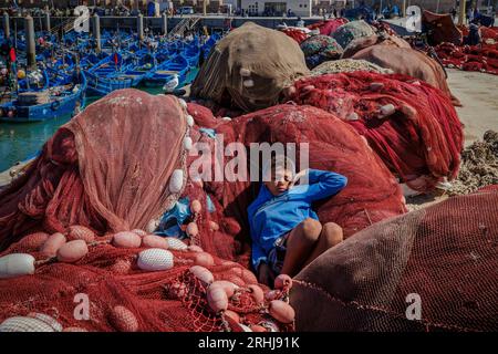 Essaouira, Morocco - August 2, 2023: Picturesque port on the Atlantic coast of Morocco, a child sleeps placidly among the fishing nets laid out on the quay. Stock Photo