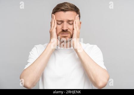 Tired man holds his head suffering from pain. Headache, migraine, overwork, illness, cold. Stock Photo