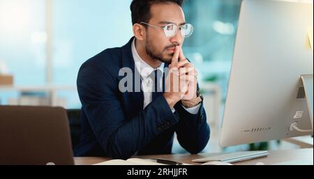 Thinking IT manager working on a desktop computer and laptop in a modern office. Information Technology software engineer analyzing data management Stock Photo