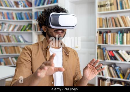 Young student close-up inside university academic library studying, man uses VR virtual reality glasses to watch course videos and online material. Stock Photo