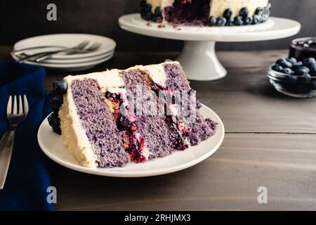 Slice of Blueberry Cobbler Cake on a Plate: Sliced 3-layer cake with blueberry crumble filling and vanilla buttercream icing Stock Photo