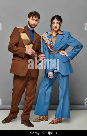 couple and fashion, models posing in formal attire, looking at camera, grey backdrop, elegant suits Stock Photo