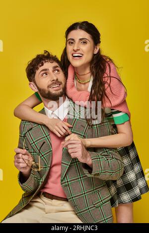 excited woman hugging bearded man, holding glasses, yellow backdrop, college outfits, students Stock Photo