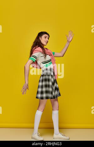 young woman acting like a doll, gesturing unnaturally, standing on yellow backdrop, student Stock Photo