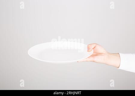 a female hand holding an empty white plate Stock Photo