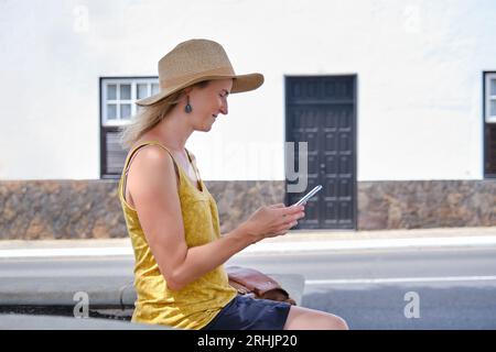 Lady using mobile phone while sitting on street in sunshine Stock Photo