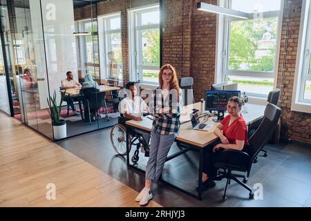 A young business group, including an African American businessman in a wheelchair, collaborates within a modern glass office, actively engaged around Stock Photo