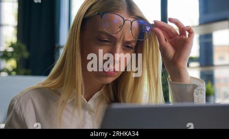 Confused Caucasian businesswoman in eyeglasses girl business woman employee take off glasses problem bad vision blurry sight reading on laptop Stock Photo