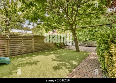 a backyard with a green lawn and wooden fenced in to the back yard there is a blue toy car parked on the grass Stock Photo