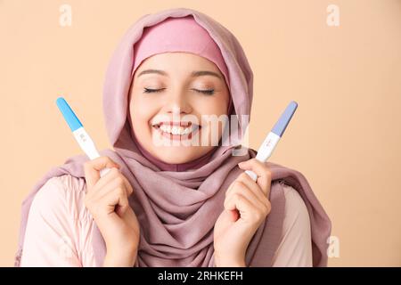 Happy Muslim young woman with positive pregnancy tests on beige background Stock Photo