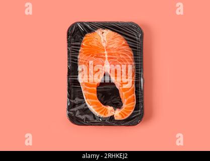 Fresh salmon steak in plastic food wrap on pink background Stock Photo