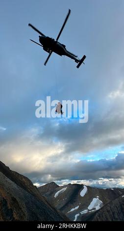 Tonsina, United States. 11 August, 2023. U.S. Air Force Staff Sgt. Nathan Weltman, a pararescueman with 57th Rescue Squadron, hoists a stranded sheep hunter from a cliff face in the remote Tonsina Controlled Use Area, August 11, 2023 near Tonsina, Alaska. Two hunters were rescued from a 6,000-foot-high cliff after becoming stranded.  Credit: Alaska Guards/US Air Force/Alamy Live News Stock Photo