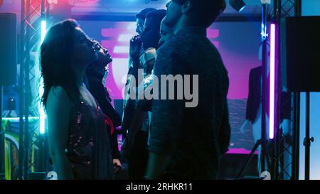 Young people jumping at dance party, funky men and women ready to show off their cool dance moves on electronic music. Happy friends having fun together at discotheque. Tripod shot. Stock Photo