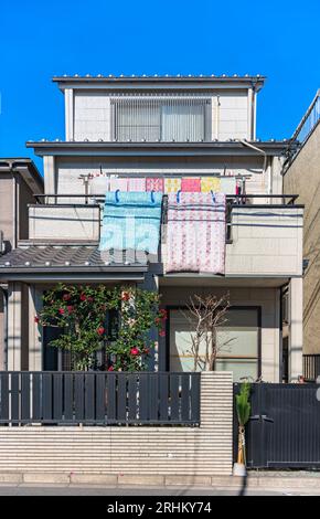 Modern Japanese house with traditional futon beds hanging on balcony in the sun to airing them and with a blooming camellia shrub and a kadomatsu deco Stock Photo
