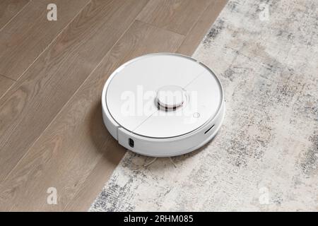 Robot vacuum cleaner on the carpet and on the laminate removes dust. The concept of a smart home, wireless cleaning with a smart vacuum cleaner Stock Photo