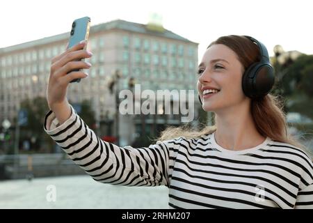 Smiling woman in headphones taking selfie on city street Stock Photo