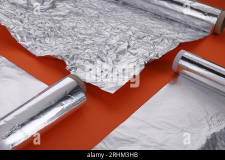 Different rolls of aluminum foil on orange background, closeup Stock Photo
