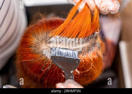 a teenage girl dyes her hair red. The process of dyeing hair red. Lightening of hair roots. Apply the brightener with a brush to the strands of hair. Stock Photo