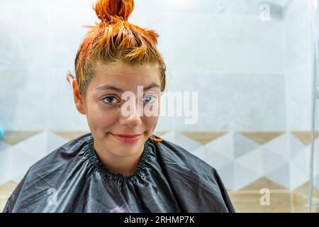 a teenage girl dyes her hair red. The process of dyeing hair red. Self-coloring of hair at home. Stock Photo