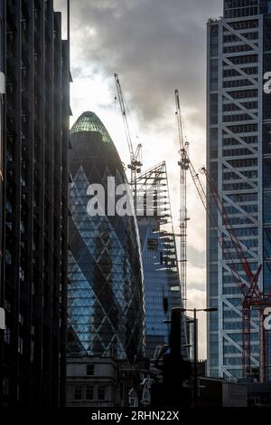 Skyscrapers and cranes in the City of London, including the Gherkin and Scalpel, silhouetted at dusk with moody sky Stock Photo