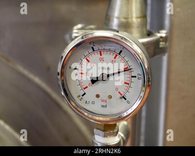 Pointer indicator of pressure on the industrial whiskey distiller construction, pipes and sensors, industrial production factory interior background Stock Photo