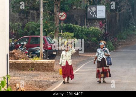 Old Goa, India - January 2023: Two Goan women walking with branches of wood on their heads on a street in Old Goa. Stock Photo