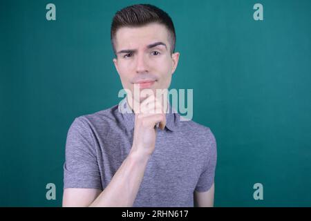 Thoughtful Handsome Young Man in Gray T-Shirt Resting Chin on Hand and Looking Towards Viewer Stock Photo