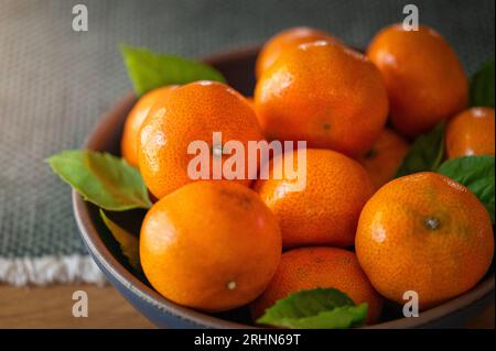 A bowl full of mandarin oranges sitting on a wood dining table Stock Photo