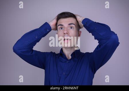 Elegant Handsome Young Man Clutches Head and Looks Up, Expression of Disbelief on Isolated Background Stock Photo
