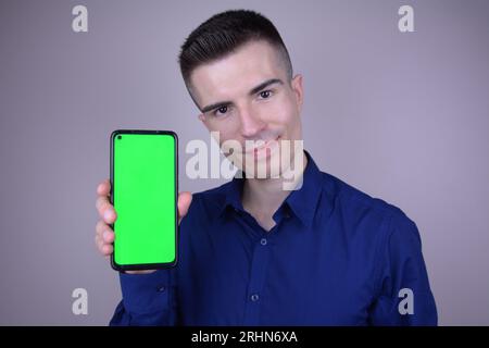 Elegant Young Handsome Smiling Caucasian Man Holding Smartphone with Green Screen Stock Photo