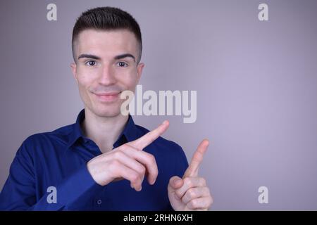 Elegant Smiling Handsome Young Caucasian Man Points Two Fingers to the Side on Isolated Background - Copy Space Stock Photo