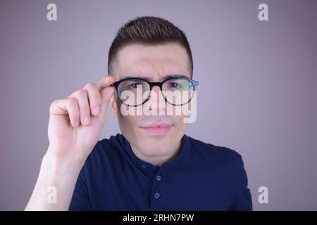 Young Man Clutches His Glasses, Looking Intently at Viewer, Isolated Background Stock Photo