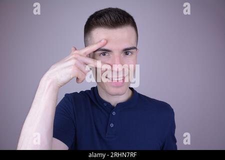 Smiling Caucasian Man with Two Fingers at Eye, Triangle Symbol on Isolated Background Stock Photo