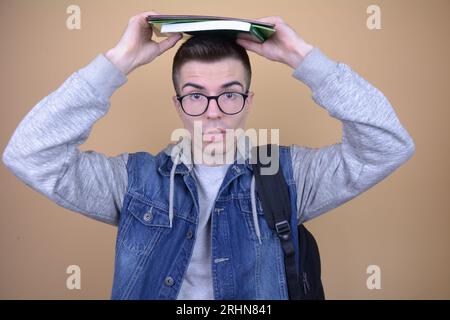 Tired Handsome Caucasian Student Balancing Textbooks and Notebooks on Head on Isolated Background Stock Photo