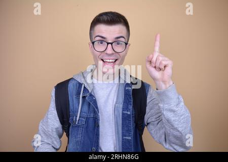 Smiling Young Handsome Caucasian Student with Glasses Has a Brilliant Idea, Pointing Upward, Wearing Backpack on Isolated Background Stock Photo
