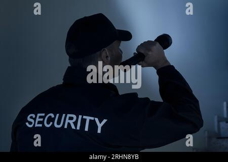 Rear view of security guard searching on stairway with flashlight in office building Stock Photo