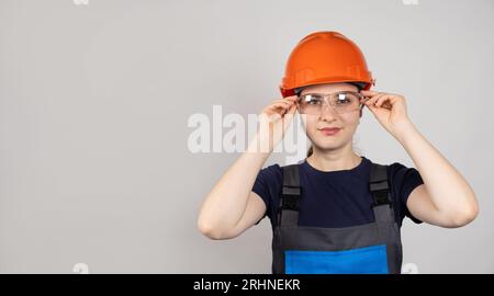 A woman in a protective helmet, glasses and overalls on a white background with space for text. Stock Photo