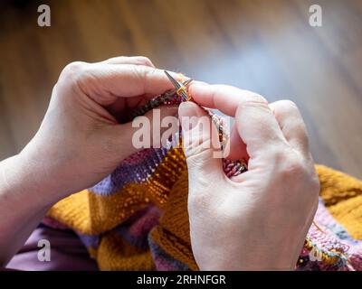 first-person view of female hands knitting sweater from woolen yarn on steel knitting needles close up Stock Photo