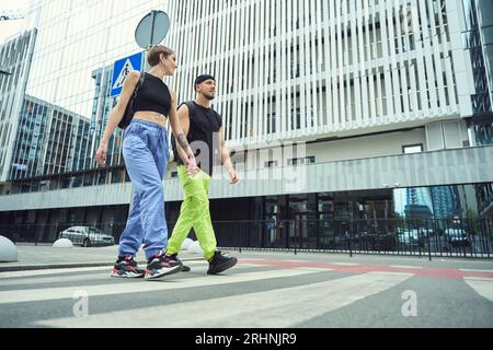 Guy with a girlfriend, holding hands, walk along pedestrian crossing Stock Photo