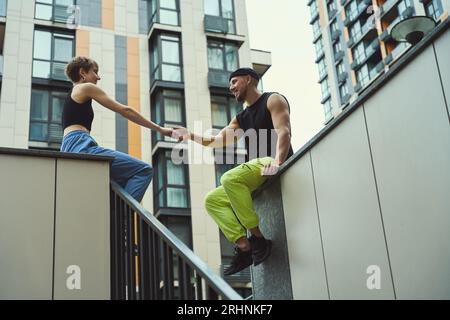 Couple of informals sits on a high curb, holding hands Stock Photo