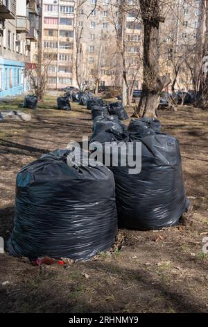 Black bags with garbage in the park, old fallen leaves, branches on the ground. A bunch of bags. Spring cleaning. City street cleaning. Stock Photo