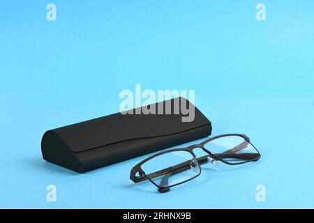 Reading glasses and black hard case isolated on blue background. High resolution photo. Full depth of field. Stock Photo