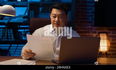 Focused middle-aged Korean businessman working online project smiling Asian man worker using corporate computer software laptop job paperwork check Stock Photo