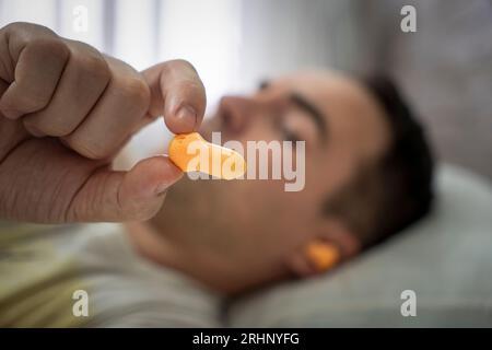beautiful young man sleeping, in ears orange earplugs against street noise, salvation from noisy neighbors. when prevent sleep. a plug in the ears for Stock Photo