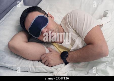 Young Man Sleeping On Bed Using blue Eye Mask. A mask for sleeping on the eyes of a sleeper during the day soaring Stock Photo